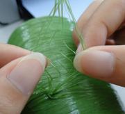Hands examining green synthetic fiber material, possibly yarn or artificial turf thread.